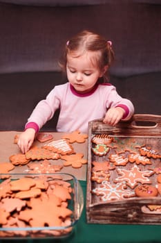 Little girl placing Christmas gingerbread cookies on wooden tray