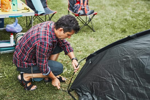 Man putting up a tent at camping during summer vacation. Preparing campsite to rest and relax. Spending vacations outdoors close to nature