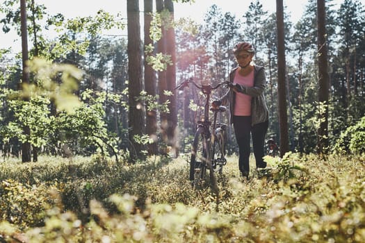 Active woman cycling on forest road. Female riding bicycle off-road route on summer vacation day. Woman wearing bicycle helmet and gloves