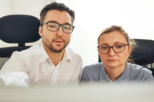 Two business people discussing financial data looking at computer screen. Entrepreneurs working hard sitting at computere screen in office. People having deadline working together. Workmates talking about project