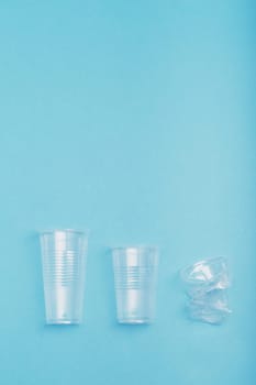 Squashed empty plastic cups put in a row, over blue background. Collecting plastic waste to recycling. Concept of plastic pollution and too many plastic waste. Copy space for text