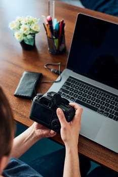 Female photographer working on photos on laptop and camera. Woman editing retouching browsing photos working as a freelancer sitting at desk