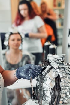 Hairdresser styling dyeing combing womans hair. Young woman working as a hairdresser in hair salon. Real people, authentic situations