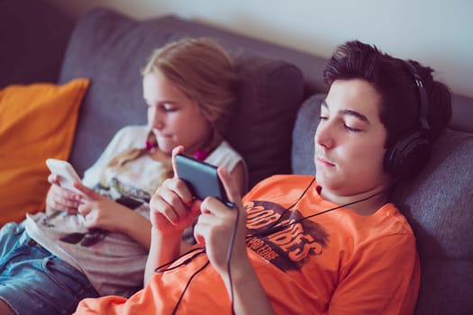 Girl and boy using smart phones, listening to music, playing the games sitting on a couch at home