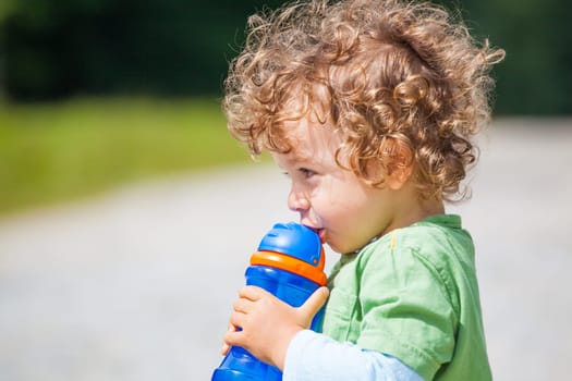 The portrait of a 1 and a half year old baby boy drinking water outdooors.