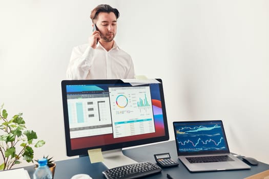 Man entrepreneur having business  conversation on mobile phone. Businessman holding documents and smartphone working with data on charts and graphs in office. Man standing at desk
