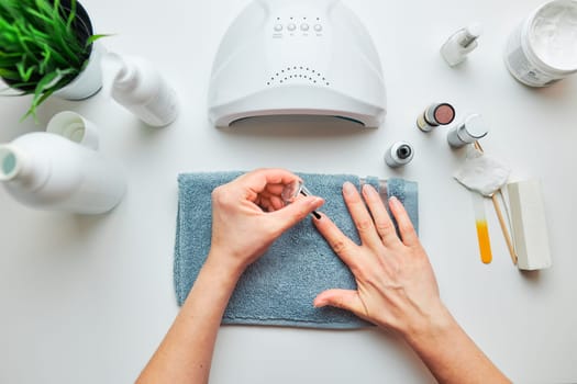 Woman preparing nails to apply gel hybrid polish using UV lamp. Beauty wellness spa treatment concept. Cosmetic products, UV lamp, green leaves on white table. Spa, manicure, skin care concept. Flat lay, overhead view