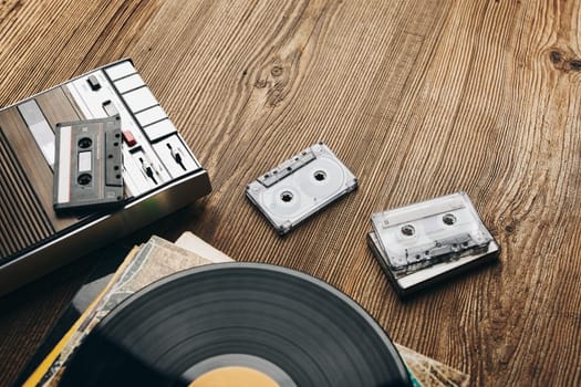 Vinyl records, cassette tapes and cassette recorder on wooden table. Retro music style. 80s music party. Vintage style. Analog equipment. Stereo sound. Back to the past