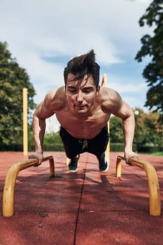 Young shirtless man bodybuilder doing push-ups on a parallel bars during his workout in a modern calisthenics street workout park