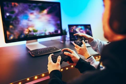Friends playing video game at home. Gamers holding gamepads sitting at front of screen. Streamers girl and boy playing online in dark room lit by neon lights. Competition and having fun