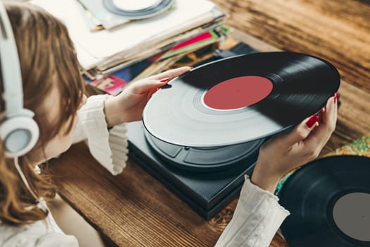 Young woman listening to music from vinyl record player. Playing music on turntable player. Female enjoying music from old record collection at home. Stack of analog vinyl records. Retro and vintage music style. Music Passion and hobby