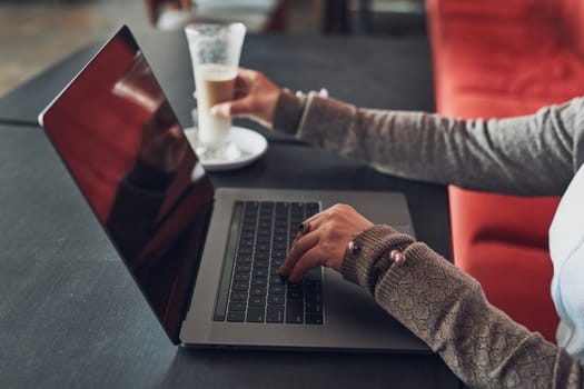Woman working remotely on her laptop computer managing her work sitting at the table in a cafe. Female hands typing on laptop keyboard
