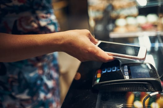 Woman paying in coffee shop using contactless method of payment via mobile phone. Woman using new way of payments