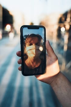 Young man having video call talking while walking downtown wearing the face mask to avoid virus infection and to prevent the spread of disease in time of coronavirus
