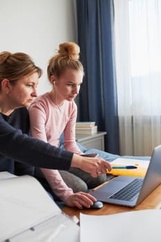 Women mother and daughter working learning remotely doing job during video chat call stream online course webinar lessons on laptop from home during COVID-19 quarantine. Women sitting on bed in front of computer looking at screen