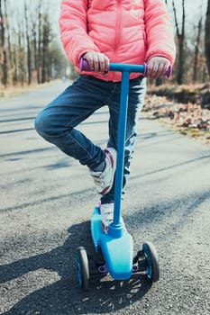 Little girl playing in the park, riding a scooter, having fun on sunny autumn day. Real people, authentic situations