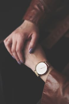 Woman wearing silver wristwatch and brown leather coat. Closeup of hands from above