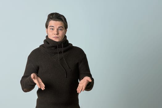 A man on a gray background in a brown sweater showing emotions, shows his hands. High quality photo
