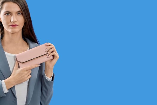 A beautiful young woman is holding a pink purse on a blue background, copy space. High quality photo