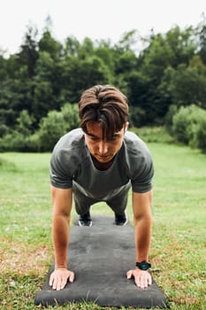 Young man doing push-ups outside on grass during his calisthenics workout. Teenager training outdoors