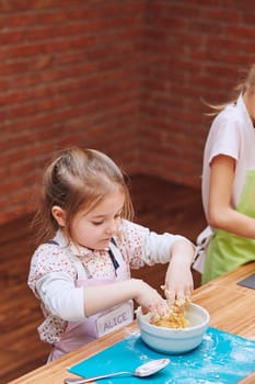Little girls kneading the dough for baking the cake. Kids taking part in baking workshop. Baking classes for children,  aspiring little chefs. Learning to cook. Combining and stirring prepared ingredients. Real people, authentic situations