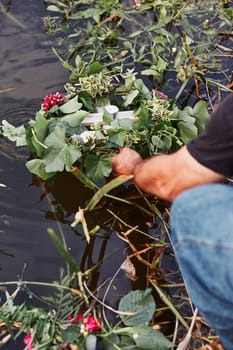 Wreaths of flowers and herbs. Man taking a wreath from a river. Midsummer divination