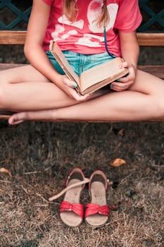 Girl reading a book, sitting on a bench in a park, relaxing outdoors