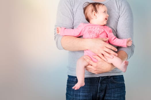 Father holding his smiling daughter. Baby is wearing pink body suit and looking at right side