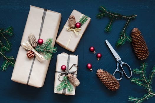 Wrapping the Christmas presents. Gifts wrapped in paper decorated with cones and pine twigs put on wooden table. View from above