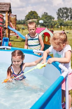 Children playing in a pool with fishing rod toy in a home garden. Kids having fun playing together on a summer sunny day