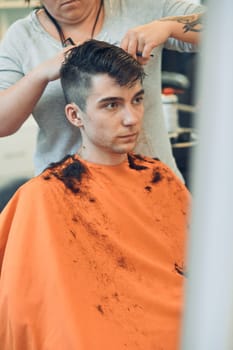 Hairdresser haircutting styling young man's hair in barbershop. Young woman working as a hairdresser in hair salon. Real people, authentic situations