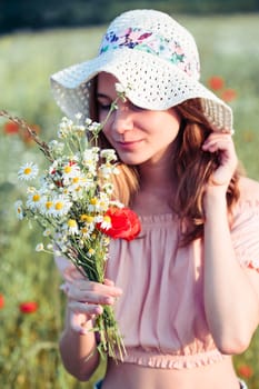 Beautieful young girl in the field of wild flowers. Teenage girl picking the spring flowers in the meadow, holding bouquet of flowers. She wearing hat and summer clothes. Spending time close to nature