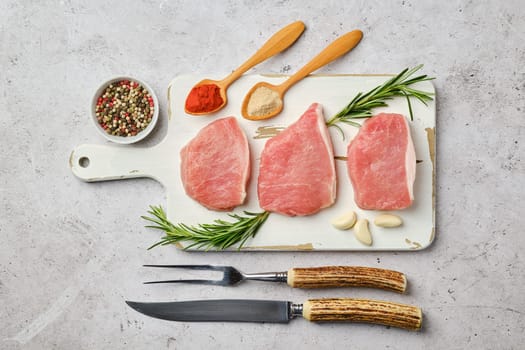 Top view of three uncooked pork cutlets on cutting board