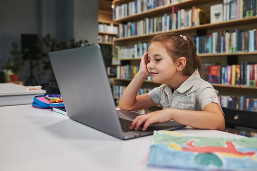 Positively engaged student doing her homework using laptop in after school club at primary school. Back to school. Child using technology on elementary computer science class. Smart little girl learning from educational application at school. Child solving riddles and puzzles on personal computer