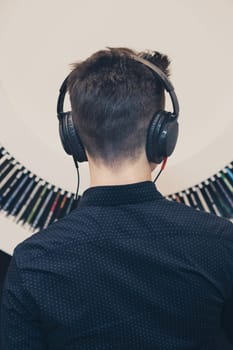 Young man listening to music through headphones standing next to bookshelf with recordings