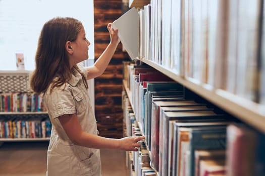 Schoolgirl choosing book in school library. Smart girl selecting books. Books on shelves in bookstore. Learning from books. School education. Benefits of everyday reading. Child curiosity. Back to school