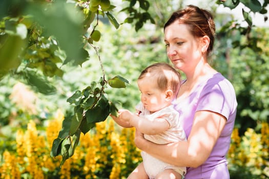 Mother showing the plant in the garden her baby girl. Relaxing outdoors close to nature