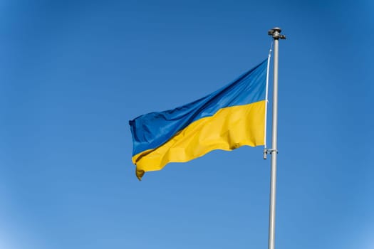 Blue-yellow Ukrainian flag flies against the background of clear blue sky.