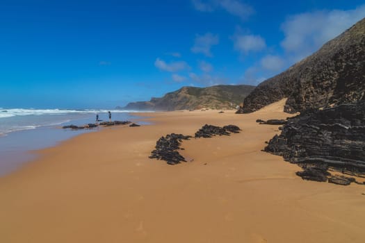 Aljezur, Portugal: 13 April, 2022: People relaxing on sand, Atlantic ocean coast, Aljezur, Portugal