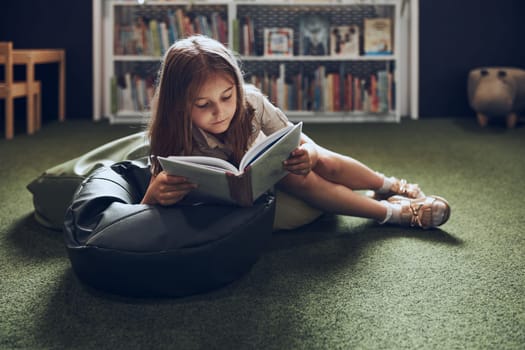Schoolgirl reading book in school library. Primary school pupil is involved in book. Child doing homework. Smart girl learning from book. Benefits of everyday reading. Child curiosity