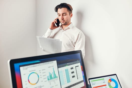 Man entrepreneur having business  conversation on mobile phone. Businessman holding documents and smartphone working with data on charts and graphs in office. Man standing at desk