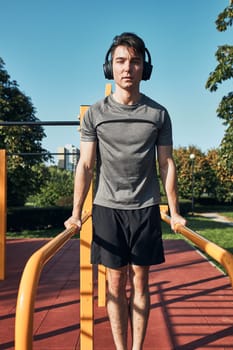 Young man doing dips on parallel bars during his workout in a modern calisthenics street workout park. Man listening to music wearing headphones and sportswear