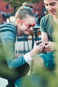 Couple of friends, teenage girl and boy,  having fun with smartphones, sitting in center of town, spending time together