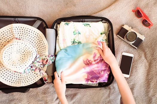 Time for summer vacation. Suitcase with packed summer clothes, a camera, a hat and sunglasses