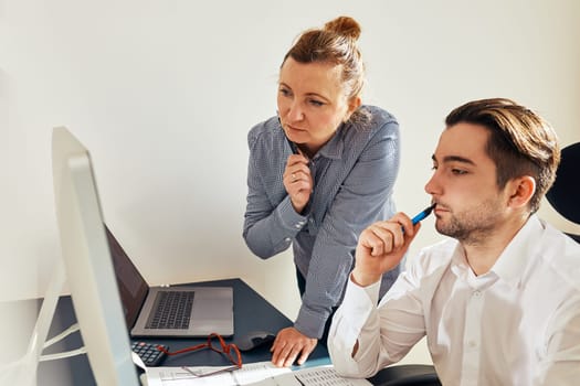 Two business people discussing financial data looking at computer screen. Businesswoman talking to young male coworker in office. People entrepreneurs having conversation working together. Workmates talking about project