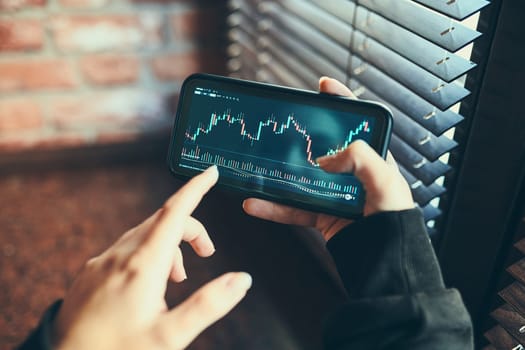 Person investing trading on stock cryptocurrency market using investing application on smartphone. Stock market investment in hand. Trader holding mobile phone looking at candle chart
