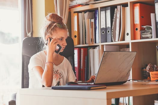 Young woman working at home, using portable computer, sitting at desk in home office. Candid people, real moments, authentic situations