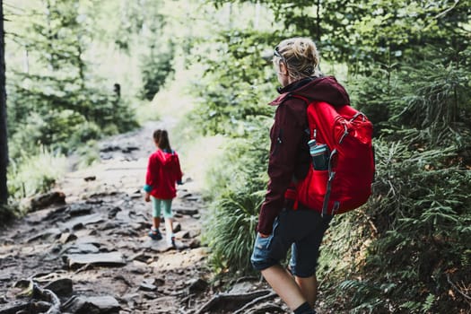 Family trip in mountains. Mother with little girl walking on path in forest, actively spending summer time together. Enjoying the outdoors in the summer trip vacation
