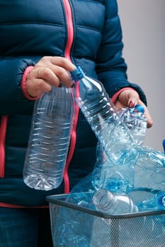 Woman throwing out used plastic bottles and packagings in trash bin. Collecting empty plastic squashed bottles in blue bag. Plastic waste to recycling. Concept of plastic pollution and too many plastic waste