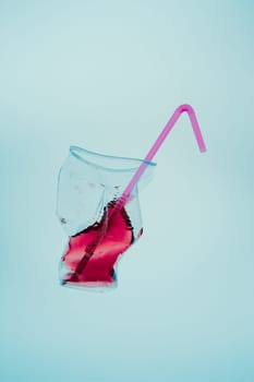 Squashed plastic cup and drink straw over blue background. Collecting plastic waste to recycling. Concept of plastic pollution and too many plastic waste. Copy space at the top